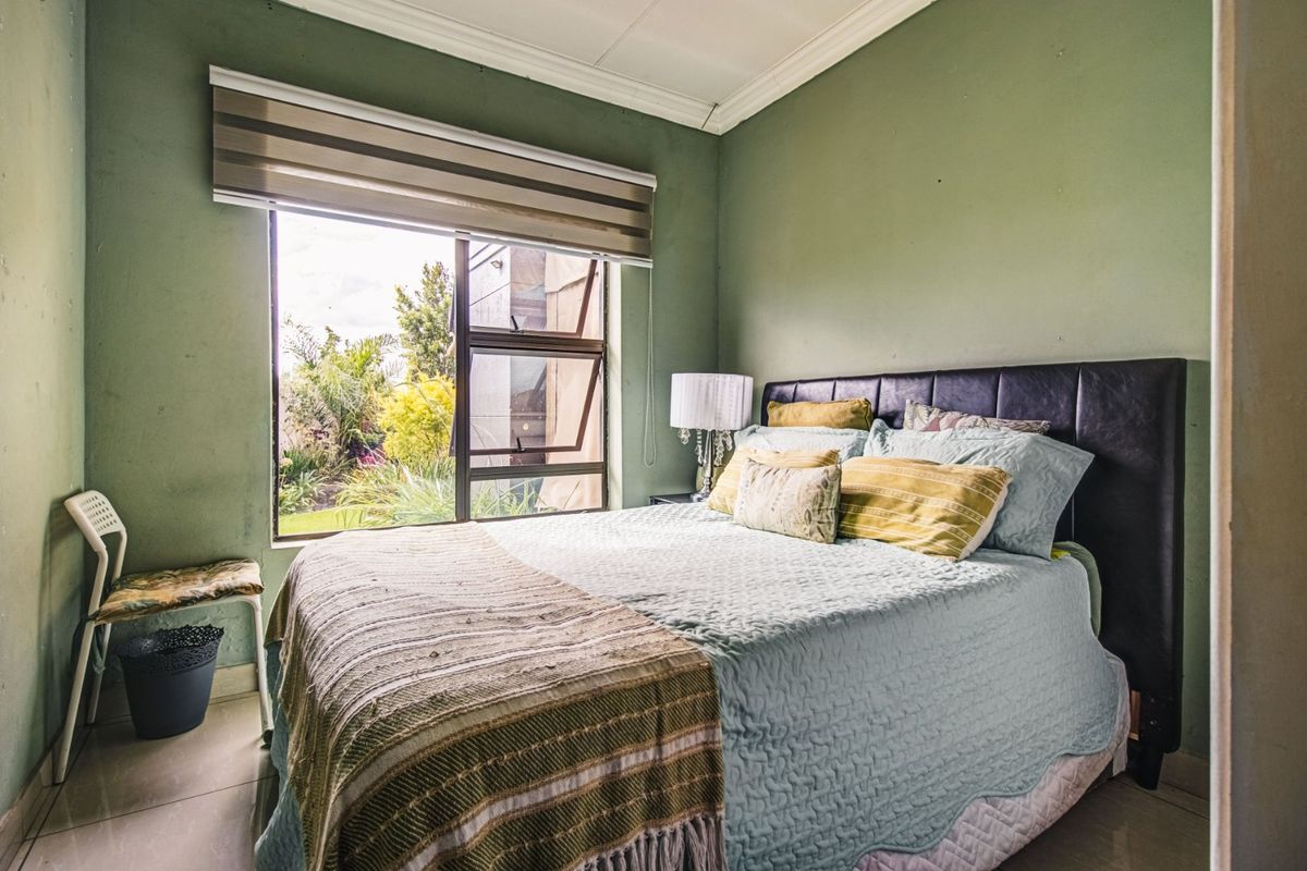 A bedroom featuring tiled flooring, an aluminium window with a roller blind, and green painted walls.