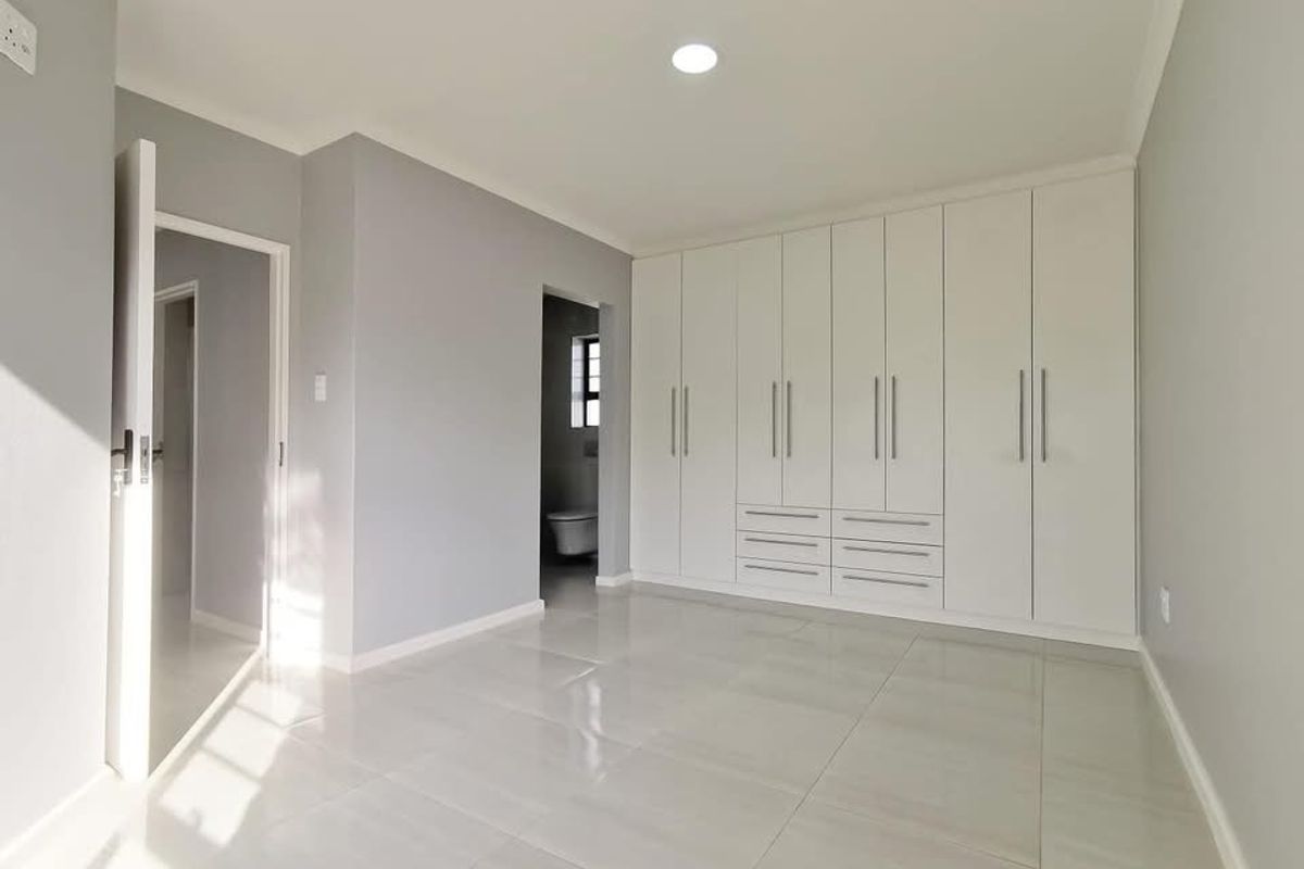 A bright, modern bedroom featuring neutral grey walls, polished tile flooring, and extensive floor-to-ceiling built-in cabinetry with integrated storage.
