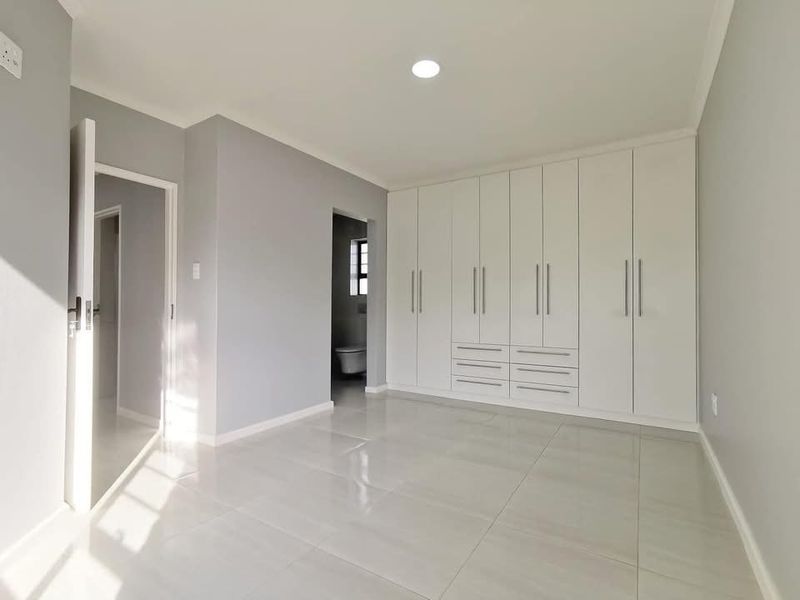 A bright, modern bedroom featuring neutral grey walls, polished tile flooring, and extensive floor-to-ceiling built-in cabinetry with integrated storage.