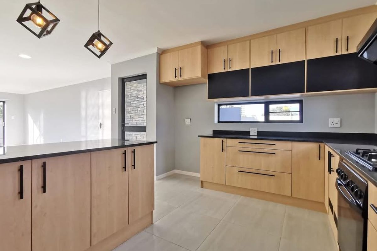 Modern kitchen featuring light wood cabinetry, contrasting black countertops, integrated gas hob, and sleek pendant lighting, seamlessly flowing into the adjacent living area.