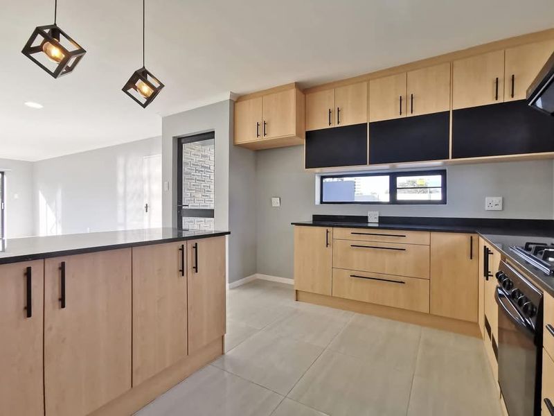 Modern kitchen featuring light wood cabinetry, contrasting black countertops, integrated gas hob, and sleek pendant lighting, seamlessly flowing into the adjacent living area.
