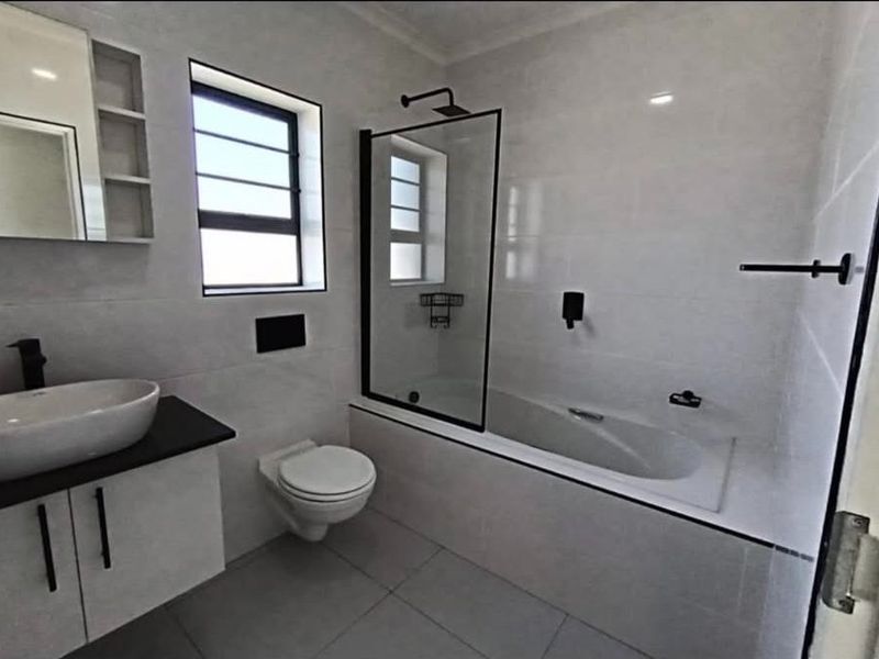 Modern bathroom featuring a wall-mounted vanity, vessel sink, bathtub with a glass shower screen, and contemporary black fixtures.