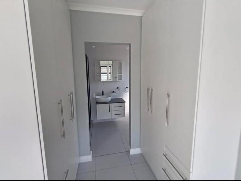 A modern dressing area featuring floor-to-ceiling built-in cupboards, leading directly into a contemporary bathroom with a floating vanity and basin.