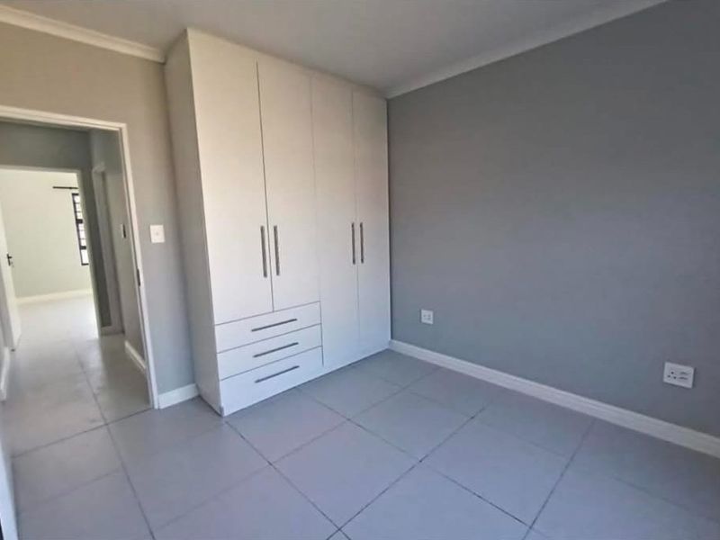 A clean, modern bedroom featuring neutral grey walls, tiled flooring, and a large built-in wardrobe with integrated drawers.