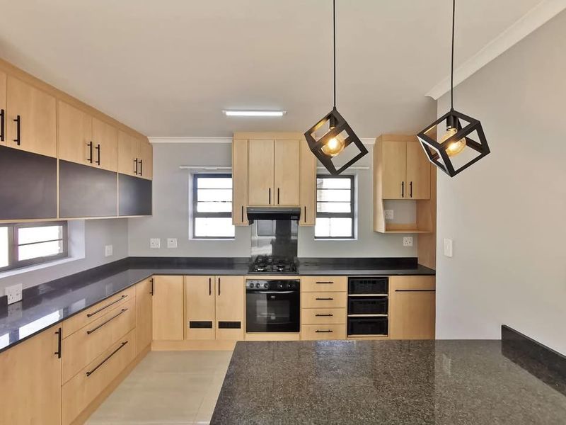 Modern kitchen featuring light wood cabinetry, dark granite countertops, built-in oven, gas hob, and contemporary pendant lighting.