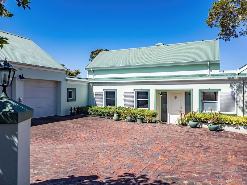 Front elevation of the property featuring a brick paved driveway, attached garage, and well-maintained exterior facade with shuttered windows.
