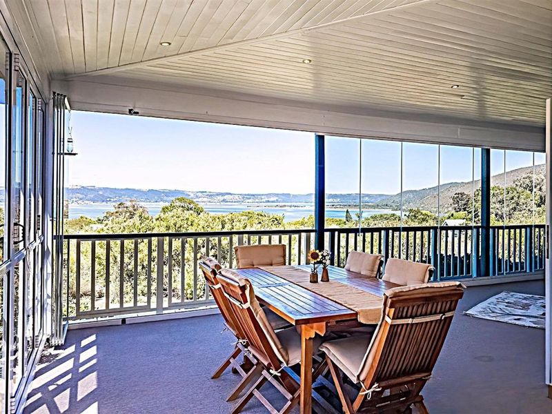 A spacious covered balcony featuring glass stacker doors, recessed lighting, and panoramic views of the surrounding landscape and water.