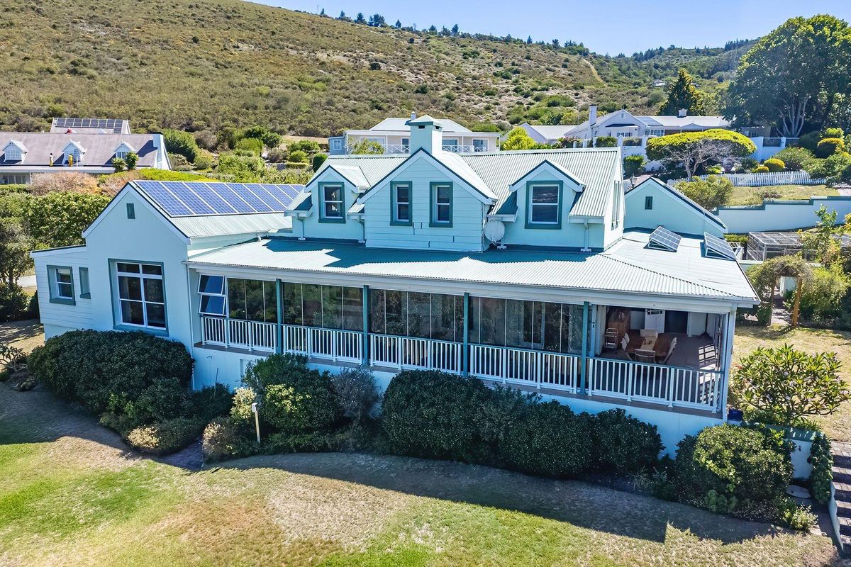 Rear view of a multi-level house featuring a large enclosed veranda, corrugated metal roofing, and integrated solar panels set against a hillside landscape.