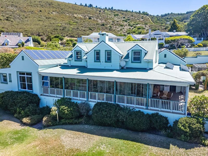 Rear view of a multi-level house featuring a large enclosed veranda, corrugated metal roofing, and integrated solar panels set against a hillside landscape.