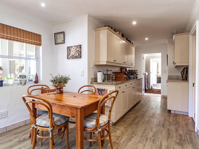 A functional kitchen featuring neutral built-in cabinetry, stone countertops, tiled splashbacks, and durable laminate flooring, with an integrated dining area.