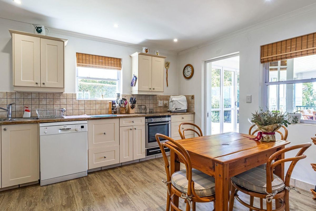 A functional kitchen featuring cream cabinetry, tiled backsplash, built-in oven, and integrated dishwasher, with direct access to an outdoor area.