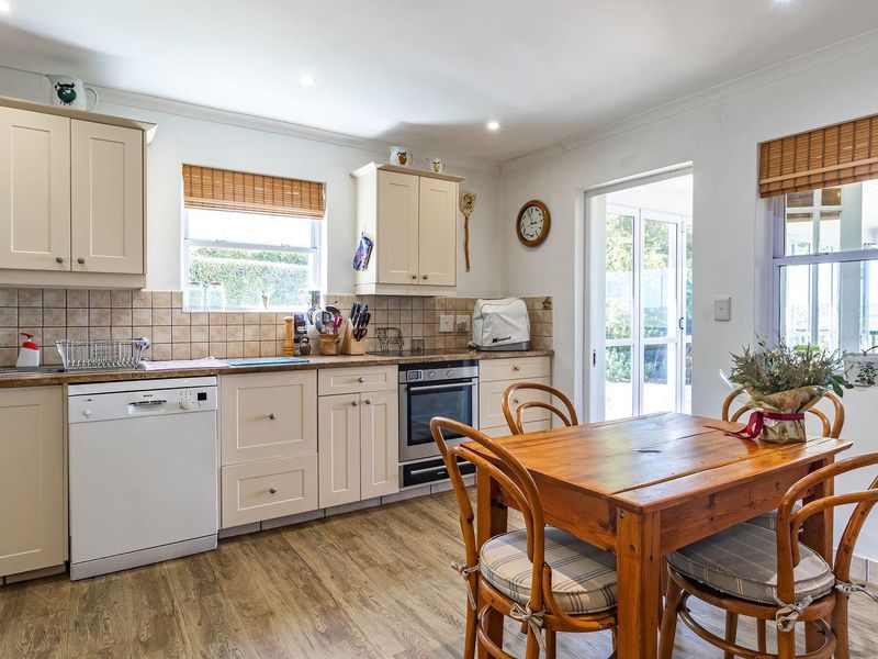 A functional kitchen featuring cream cabinetry, tiled backsplash, built-in oven, and integrated dishwasher, with direct access to an outdoor area.