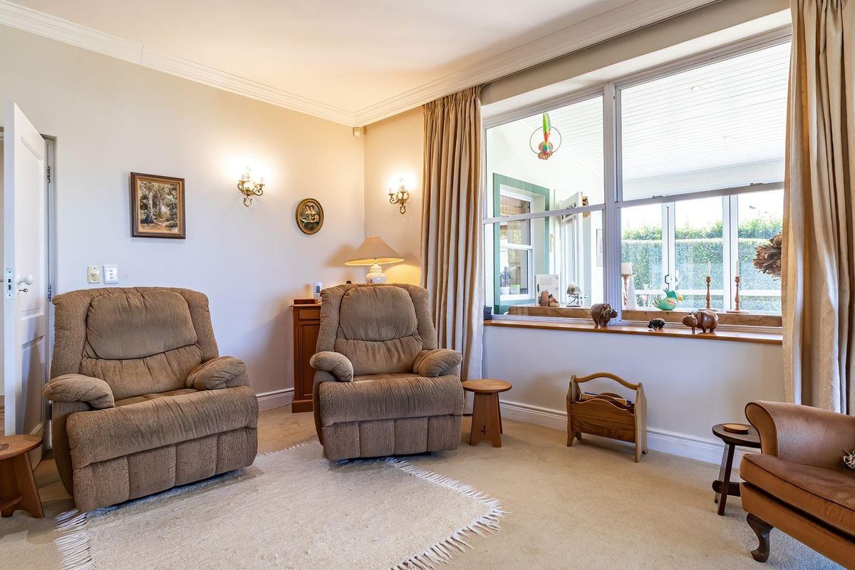 A comfortable living room featuring crown molding, wall sconces, and a large window that provides natural light and views into the adjacent sunroom.