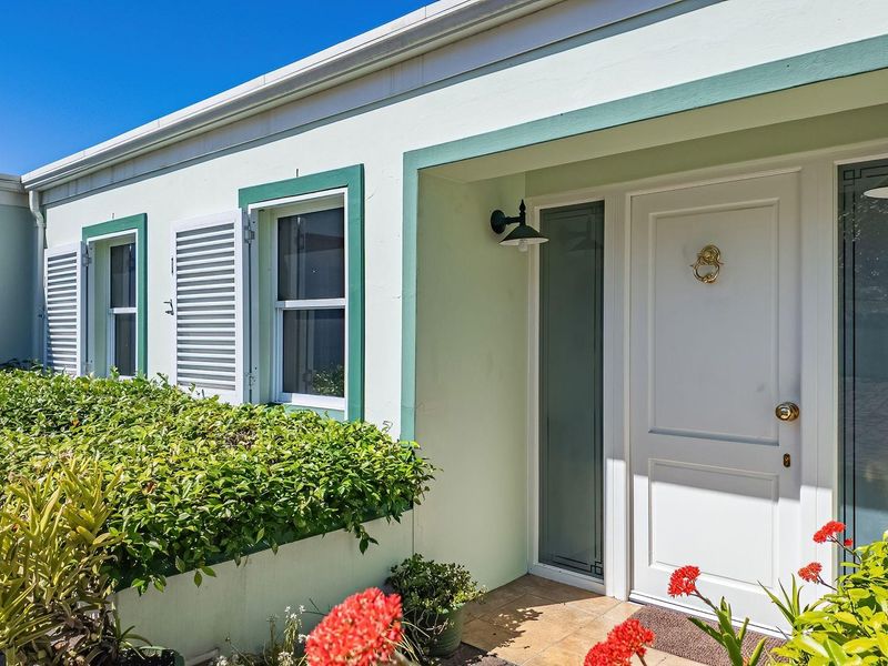 A well-maintained front entrance featuring a classic white door, green-trimmed windows with shutters, and a tiled porch area.
