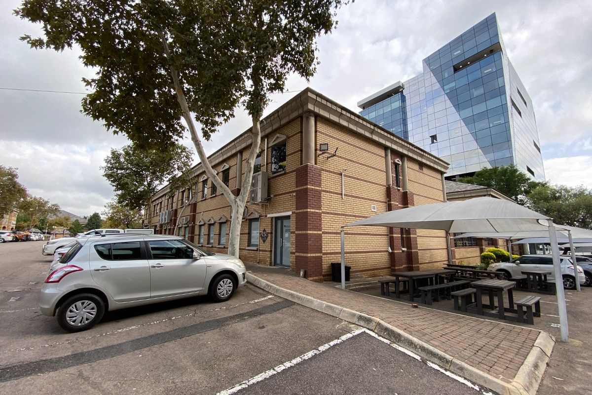 Exterior view of a commercial brick building featuring a paved parking area and a covered outdoor seating space.