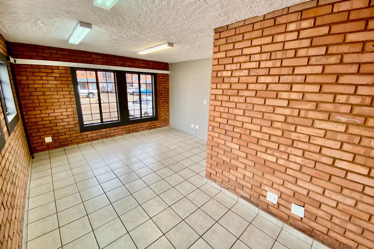 An empty office space featuring exposed brick walls, ceramic tile flooring, and functional fluorescent lighting, suitable for a variety of industrial or commercial uses.
