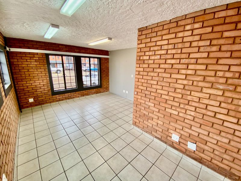 An empty office space featuring exposed brick walls, ceramic tile flooring, and functional fluorescent lighting, suitable for a variety of industrial or commercial uses.