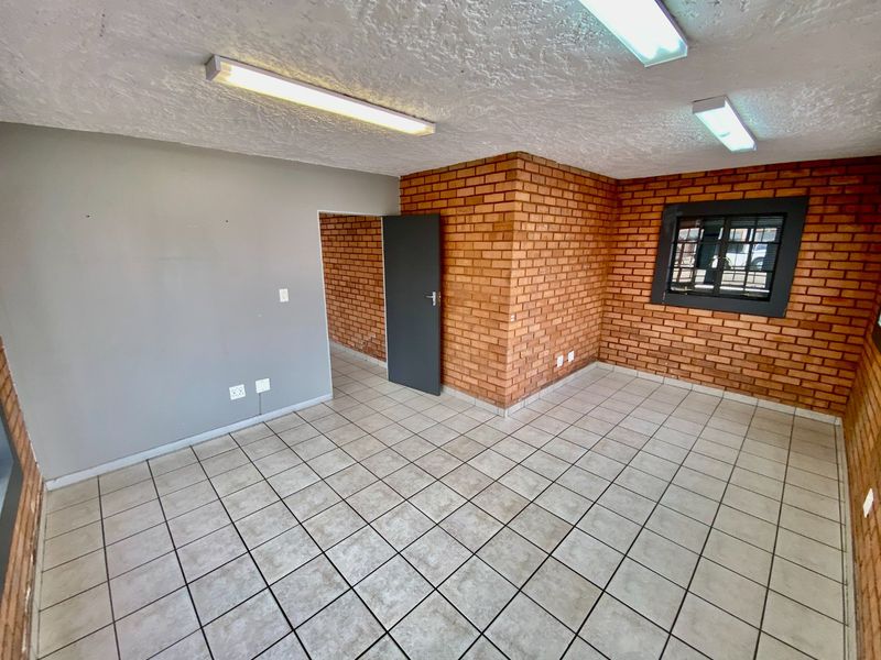 An empty office space featuring exposed brick walls, ceramic floor tiles, and functional fluorescent lighting, suitable for a variety of industrial or commercial uses.