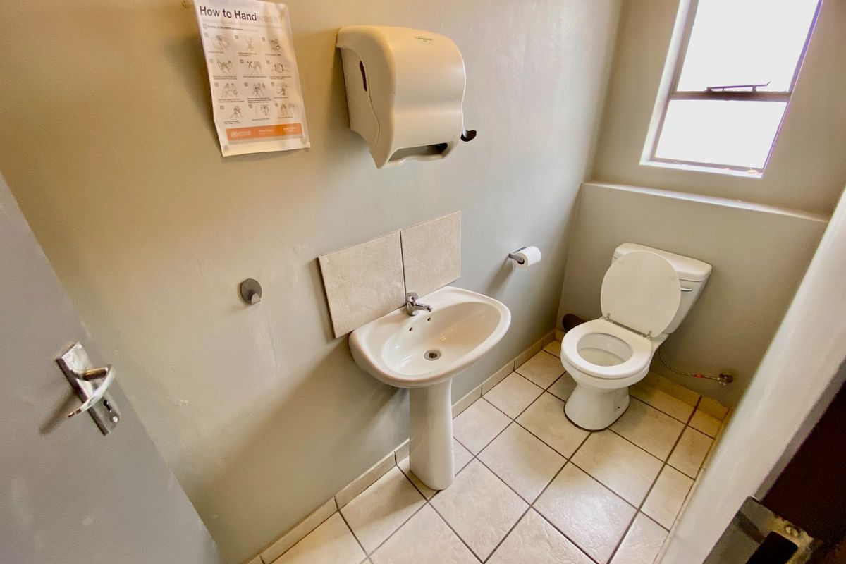 A functional industrial-style restroom featuring a pedestal basin, toilet, and tiled flooring with neutral wall finishes.
