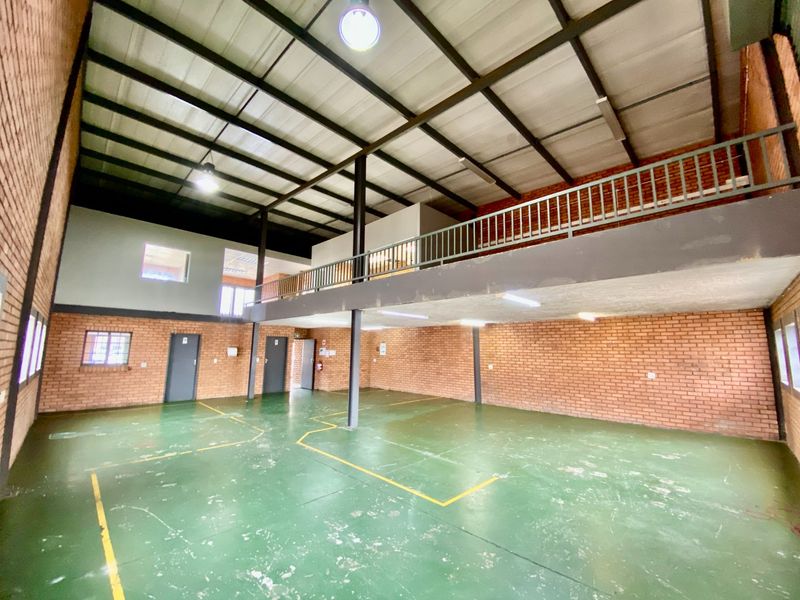 Spacious industrial utility area featuring high ceilings, exposed brickwork, a mezzanine level with metal railing, and durable painted concrete flooring.