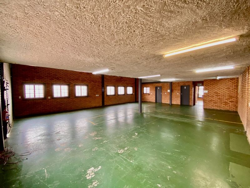Spacious industrial utility area featuring exposed brick walls, painted concrete flooring, and functional fluorescent lighting, suitable for storage or workshop use.