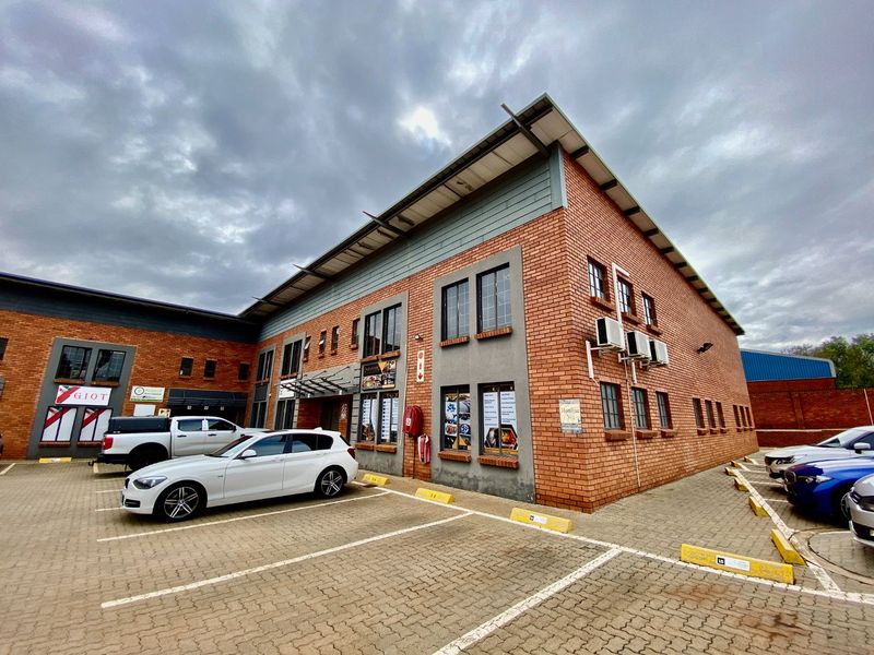 A multi-story industrial building featuring a face brick facade, paved parking area, and external air conditioning units.
