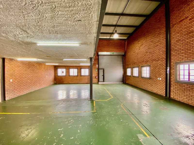 Spacious industrial utility area featuring exposed brick walls, high ceilings with exposed steel beams, a large roller shutter door, and durable painted concrete flooring.