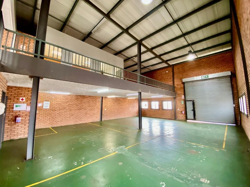 Spacious industrial warehouse unit featuring a mezzanine level, high ceilings with exposed steel beams, roller shutter access, and durable painted concrete flooring.
