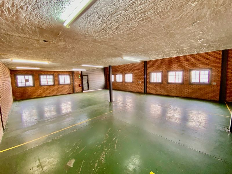 Spacious industrial utility area featuring exposed brick walls, painted concrete flooring, fluorescent lighting, and a large roller shutter door for easy access.