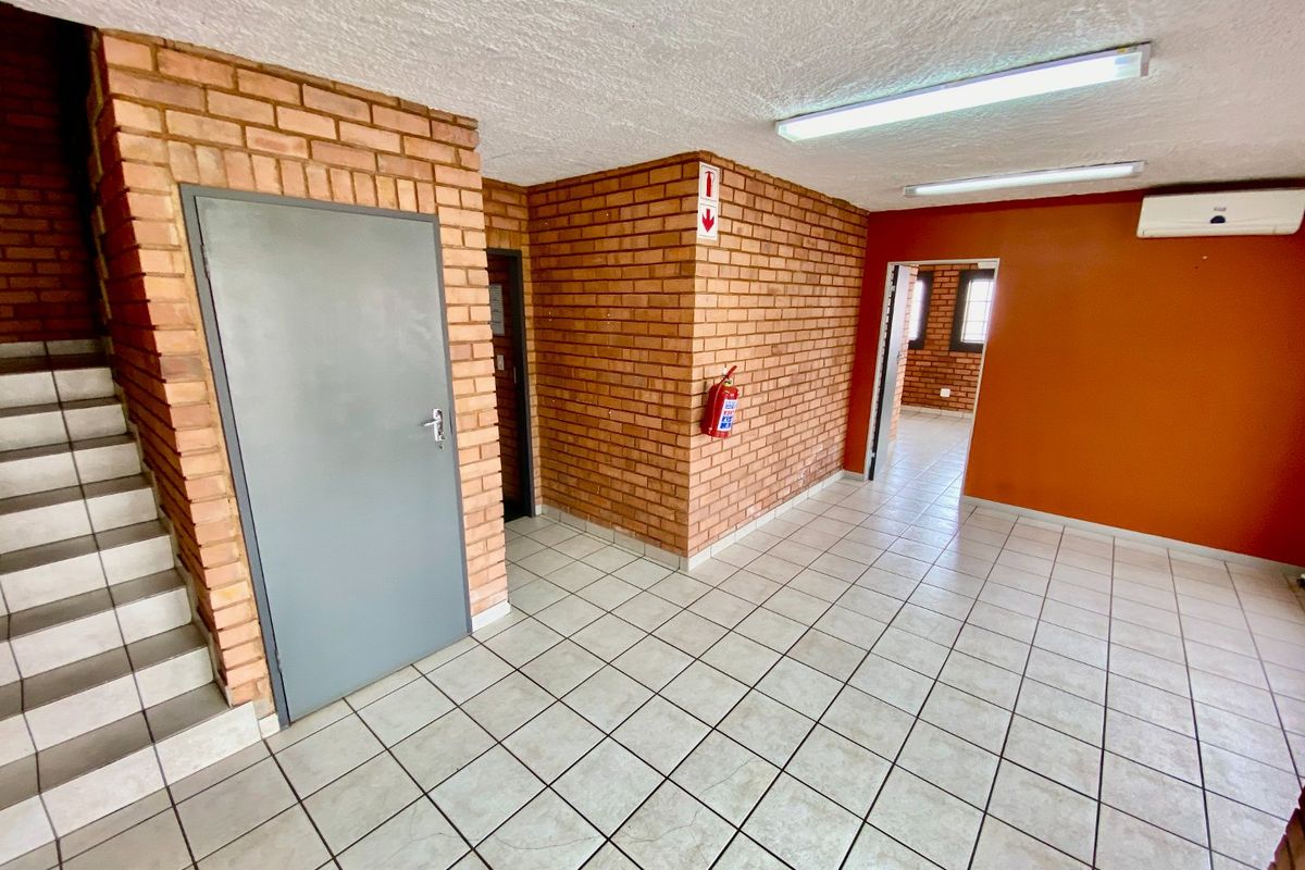 Spacious industrial hallway featuring exposed brick walls, tiled flooring, and integrated air conditioning, providing access to multiple office or utility areas.