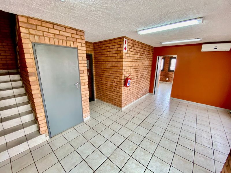 Spacious industrial hallway featuring exposed brick walls, tiled flooring, and integrated air conditioning, providing access to multiple office or utility areas.
