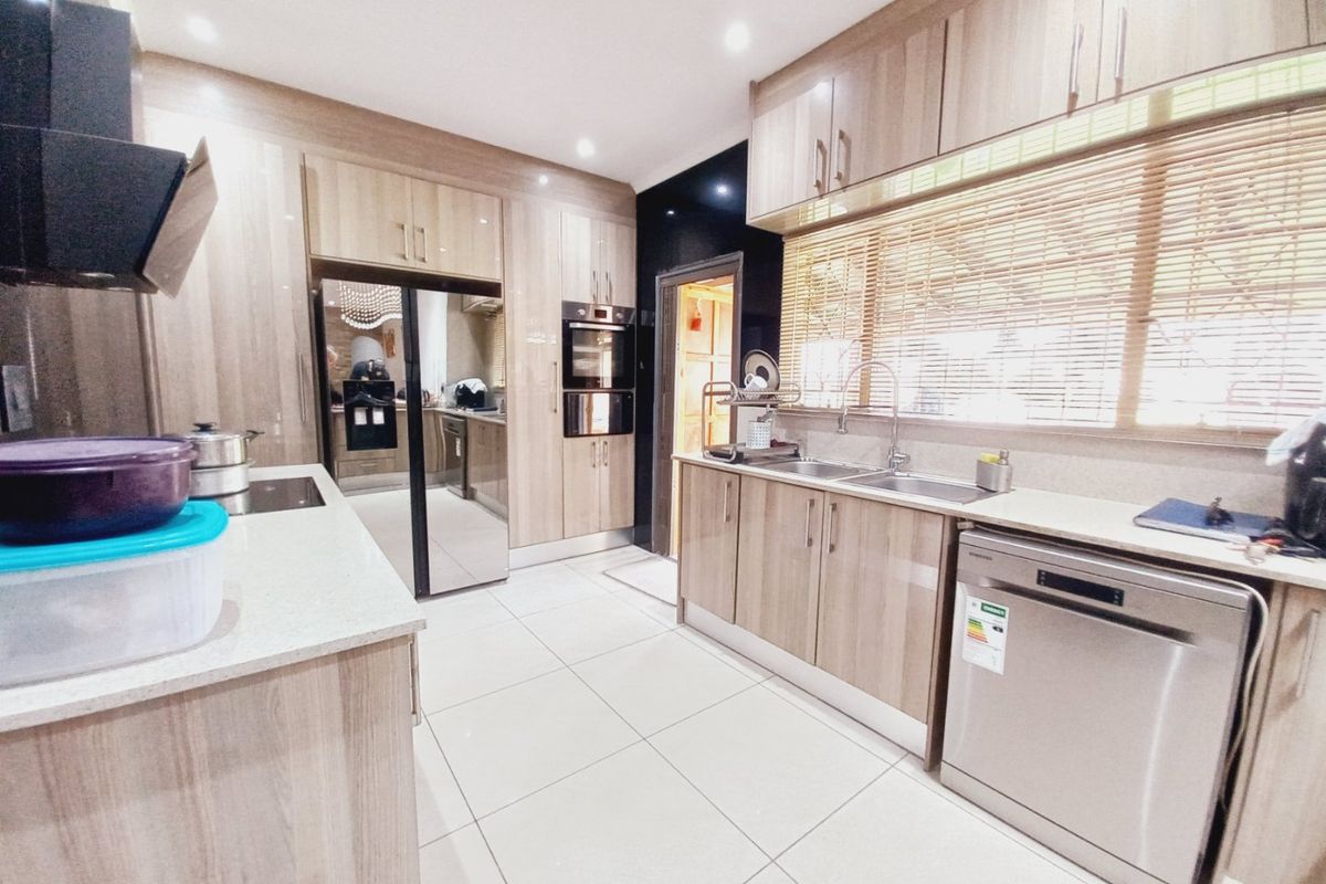 Modern kitchen featuring light wood-grain cabinetry, stone countertops, integrated appliances, double sink, and tiled flooring with ample storage space.