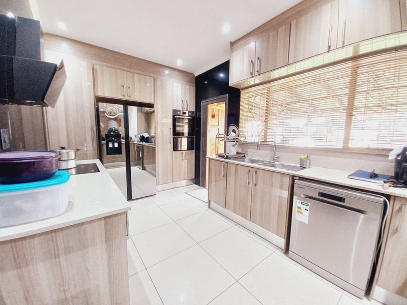 Modern kitchen featuring light wood-grain cabinetry, stone countertops, integrated appliances, double sink, and tiled flooring with ample storage space.