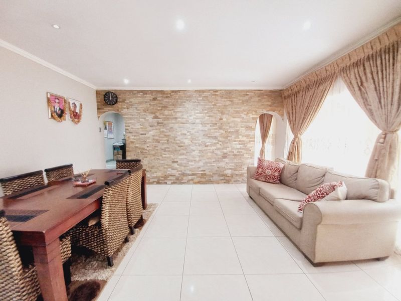 Spacious open-plan living and dining area featuring a textured stone feature wall, neutral tiled flooring, and elegant arched architectural details.
