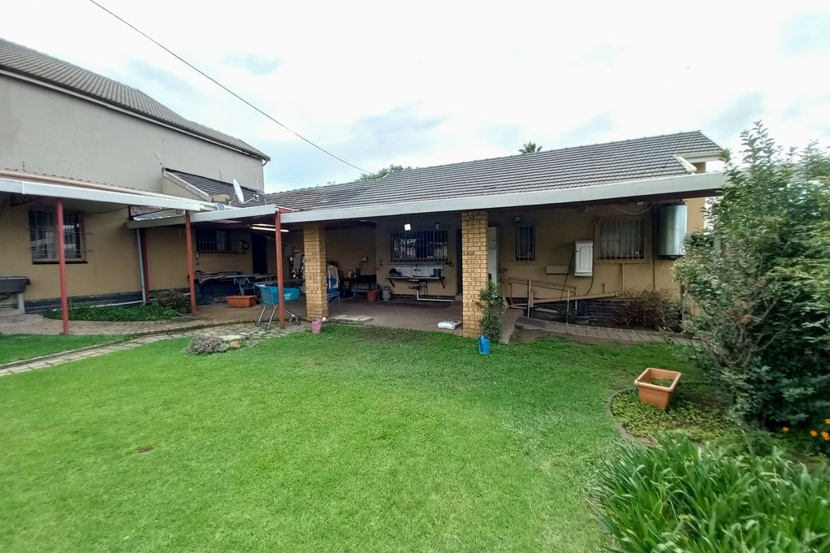 Rear view of the property featuring a covered patio area, brick pillars, and a spacious garden with paved walkways.