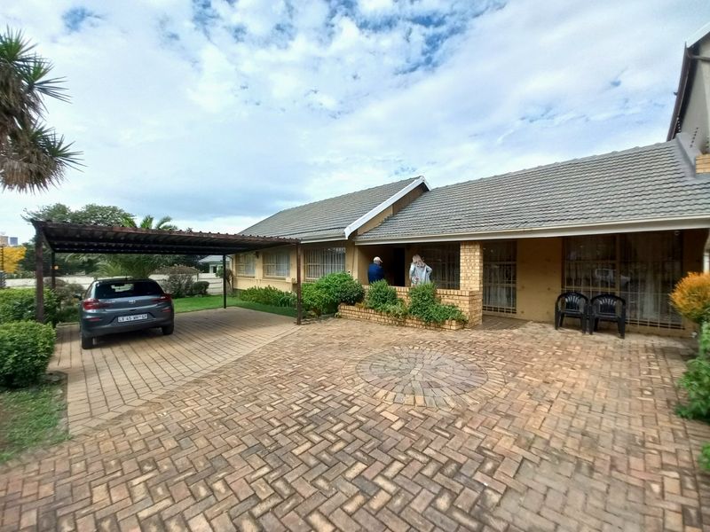 Front exterior view of a single-story house featuring a paved driveway, carport, and brick facade with security gates.