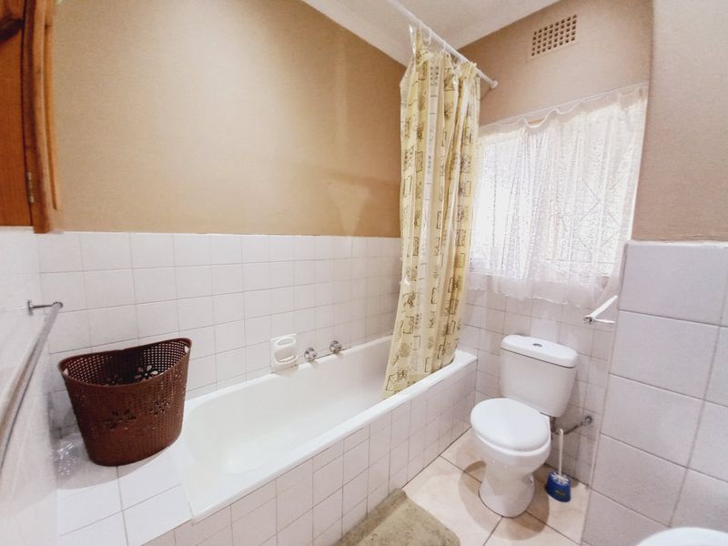 A functional bathroom featuring a built-in bathtub with shower curtain, standard toilet, and tiled finishes throughout.
