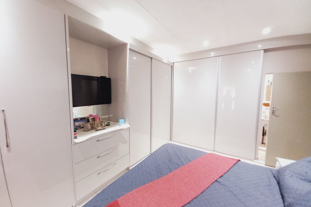 A well-maintained bedroom featuring extensive built-in wardrobes with high-gloss finishes and integrated vanity storage.