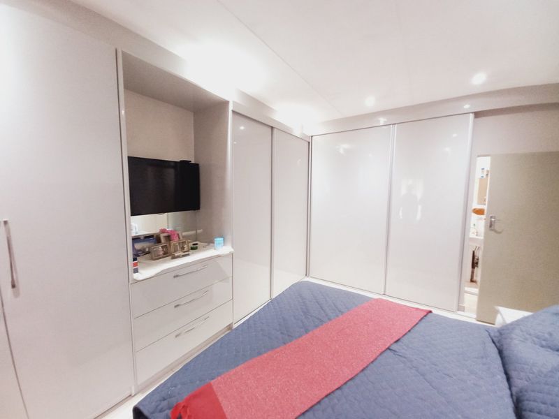A well-maintained bedroom featuring extensive built-in wardrobes with high-gloss finishes and integrated vanity storage.