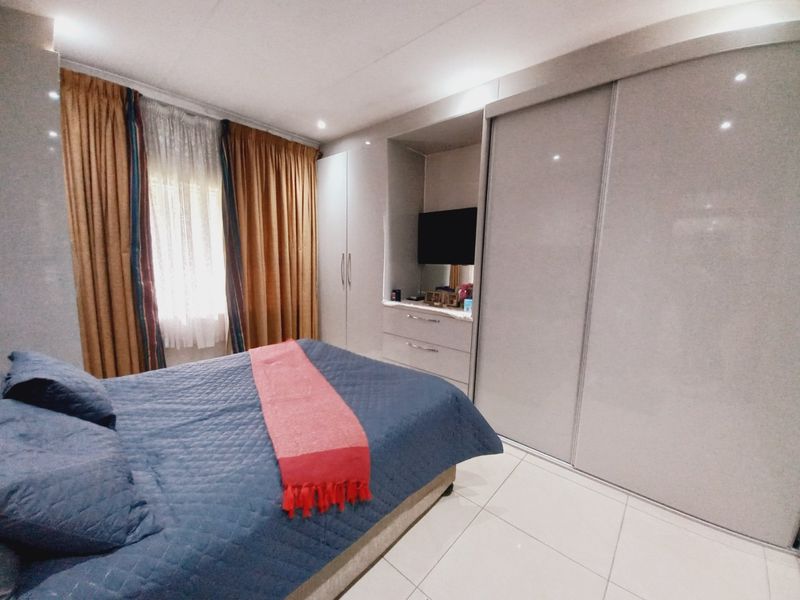 A well-maintained bedroom featuring modern built-in cupboards with a glossy finish, tiled flooring, and recessed ceiling lighting.