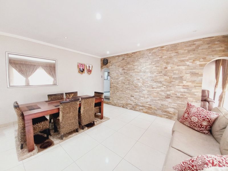 Open plan living and dining area featuring a prominent stone feature wall, neutral tiled flooring, and recessed lighting.
