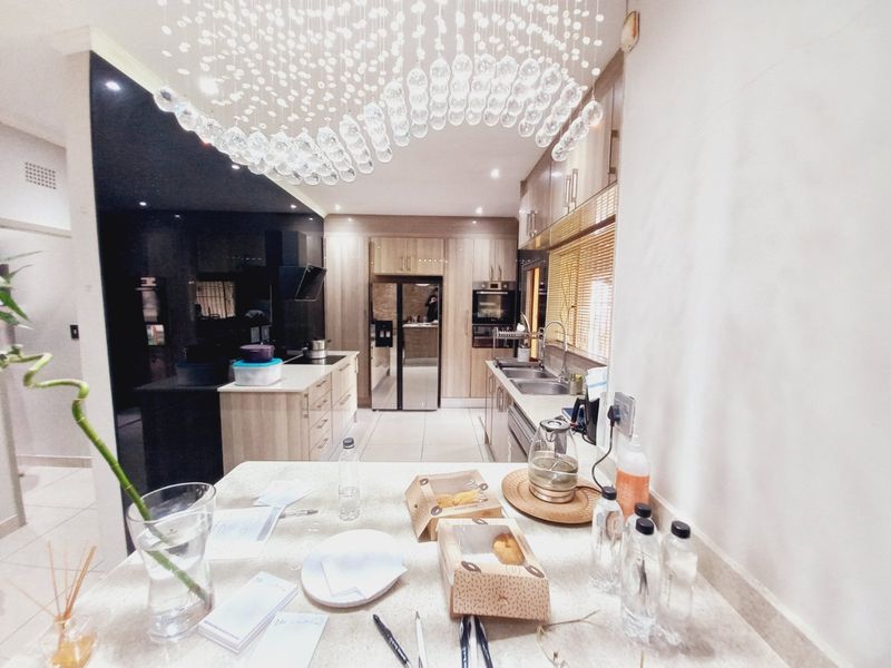 Modern kitchen featuring light wood cabinetry, stone countertops, integrated appliances, and a striking contemporary chandelier over the central island.
