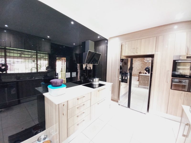 Modern kitchen featuring light wood cabinetry, a central island with integrated hob, sleek black splashback, and built-in oven appliances.