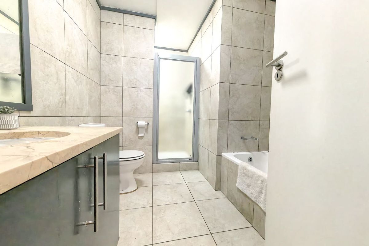 A functional bathroom featuring a vanity with stone countertop, a separate shower enclosure, and a bathtub with full-height wall tiling.