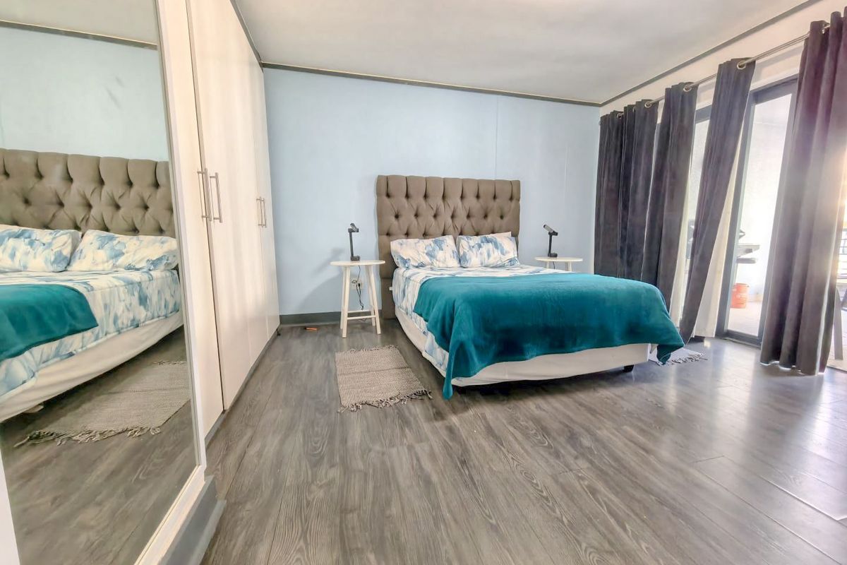 Spacious bedroom featuring modern laminate flooring, built-in mirrored wardrobes, and direct access to an outdoor area through sliding glass doors.