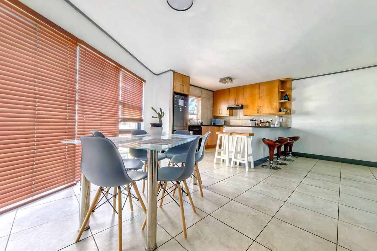 Open-plan kitchen and dining area featuring tiled flooring, wooden cabinetry, and large windows with venetian blinds, creating a functional and bright living space.