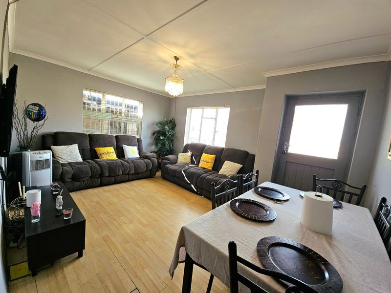 An open-plan living and dining area featuring light-toned flooring, neutral walls, and a central chandelier, providing a functional space for daily living.
