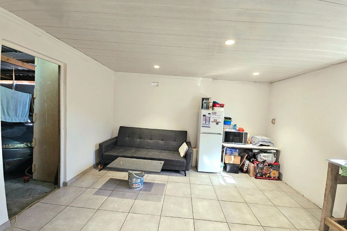 A multi-purpose living area featuring tiled flooring and a panelled ceiling, currently used as a combined lounge and utility space.