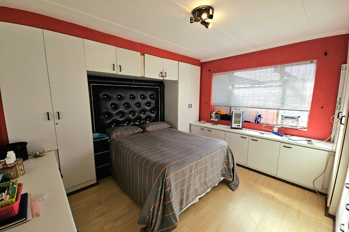 A bedroom featuring extensive built-in white cabinetry and overhead storage units, complemented by laminate flooring and a large window with fitted blinds.