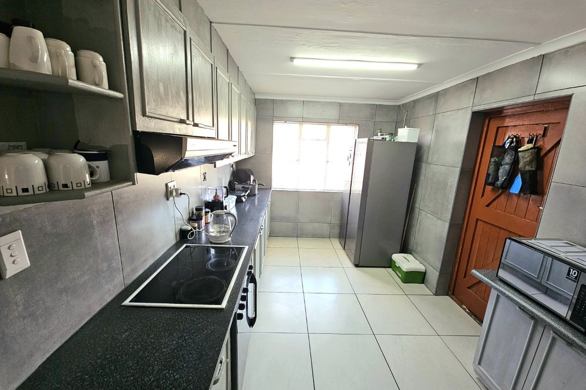 A functional galley-style kitchen featuring tiled walls, dark countertops, a built-in electric hob, extractor fan, and ample cabinetry for storage.